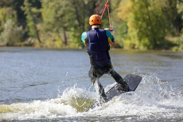 Young man surfing on the pond, is pulled by a cable machine