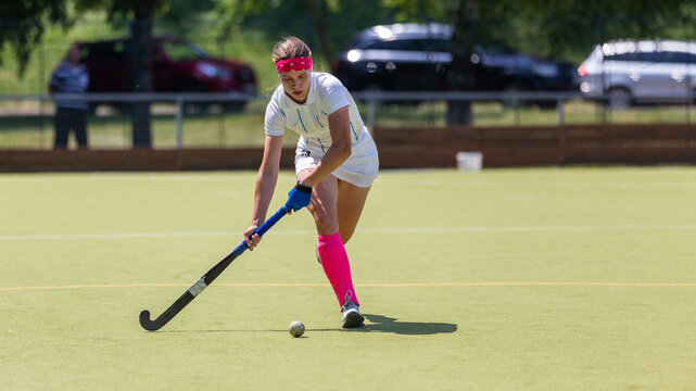 Young female player running with ball in attack on the pitch in field hockey game