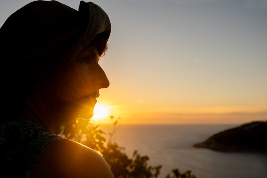 Frau mit Hut schaut bei Sonnenuntergang auf den Golf von Thailand.
