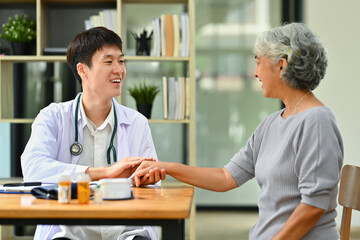 Smiling doctor in white coat holding hand, supporting senior female patient. Medical healthcare concept