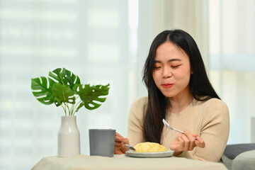 Happy young asian woman in casual clothes having breakfast at home. Concept of wellness, food and domestic lifestyle