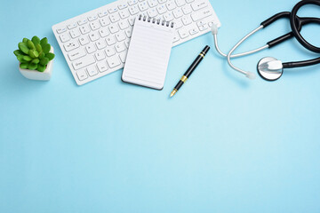 Stethoscope, computer keyboard, pen, note pad, and greenery on a blue background.