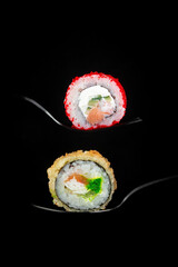 Sushi rolls on a fork and spoon on a dark background