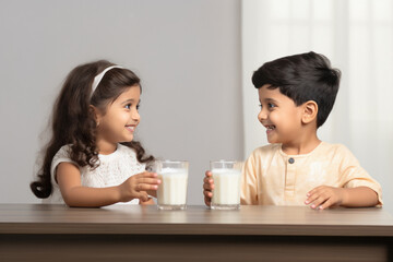 Indian little siblings drinking milk in glass - obrazy, fototapety, plakaty