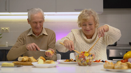 A senior couple preparing breakfast meal, spreading fresh butter on a crispy baguette, and making a salad