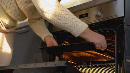 A woman putting a baking pan in the oven, preparing a delicious meal for a family dinner