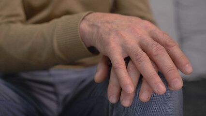 Close-up of a senior male hands on his knees, trembling in old age, neurological disorders