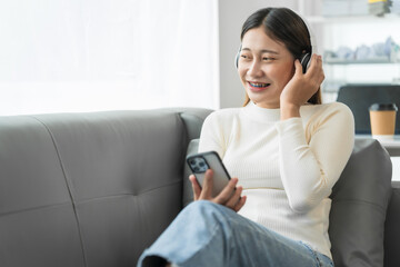 Asian woman with braces sits online shopping on sofa with laptop. mobile phone and credit card in...