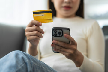Asian woman with braces sits online shopping on sofa with laptop. mobile phone and credit card in hand