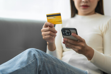 Asian woman with braces sits online shopping on sofa with laptop. mobile phone and credit card in hand