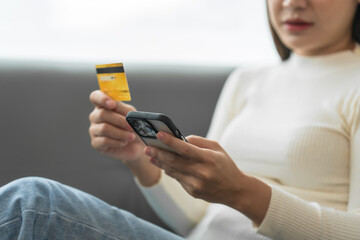 Asian woman with braces sits online shopping on sofa with laptop. mobile phone and credit card in hand