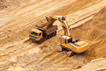 excavator extracts and loads sand into large truck in sand quarry