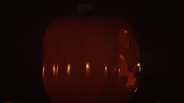 Halloween pumpkin smile and scary eyes with burning candle inside rotating at darkness background. Spooky face glowing in dark