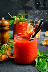 Fresh tomato juice with spices and basil in a cup. On a dark stone table.