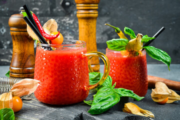Glass of tomato alcoholic cocktail with spices and basil. On a dark stone table.