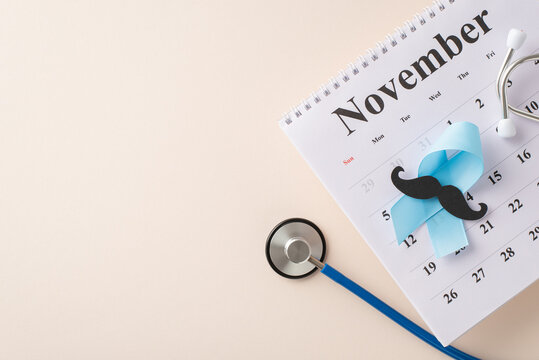 Raising awareness for Men's Health Month. Overhead image of blue ribbon, mustache silhouette, stethoscope, and November calendar on a pastel beige background, representing health checkup planning