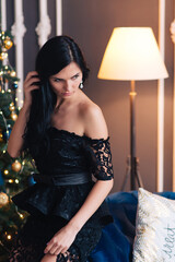 Happy smiling woman in black lace evening dress, caucasian, christmas tree bokeh lights in background. New Year and Christmas in the interior.