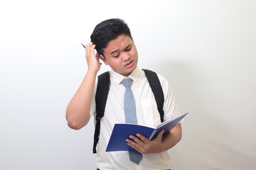 Indonesian senior high school student wearing white shirt uniform with gray tie writing on note book using pen with annoyed and frustrated expression. Isolated image on white background