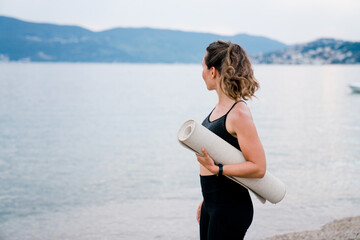 Woman with yoga mat on beach. Girl preparing to sport workout in nature by sea. Concept of healthy lifestyle, morning exercises and fitness, female wellness and healthcare, activities outdoors