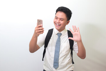 Indonesian senior high school student wearing white shirt uniform with gray tie waving his hand to...