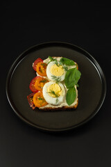 Sandwich with boiled egg and tomatoes. Sandwich on a plate. Black plate and dark background.