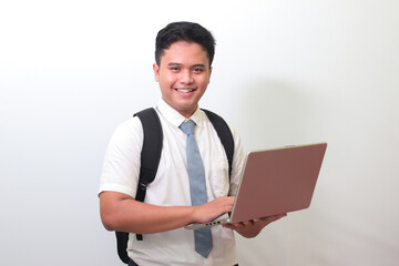Indonesian senior high school student wearing white shirt uniform with gray tie holding a laptop, standing against gray background