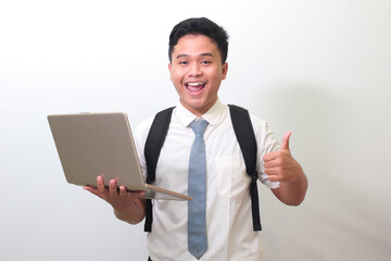 Indonesian senior high school student wearing white shirt uniform with gray tie holding a laptop...
