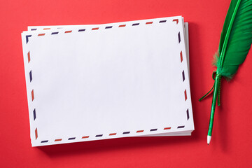 A stack of white empty mailing envelopes and a pen in the shape of a feather on a red background, template for the designer