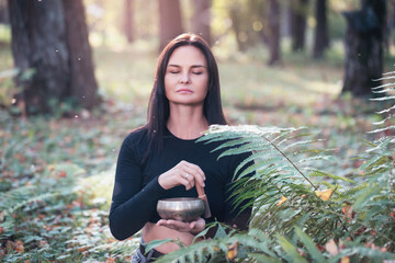 Woman practicing yoga, doing sound meditation with a Tibetan bowl, relieves stress and improves the...