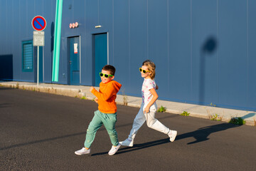 Cheerful smiling children, boy and girl 7 and 8 years old in bright sunglasses playing tag on the street - 658601017