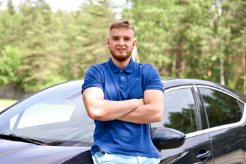 Young happy handsome man driver standing near his new car with his hands crossed