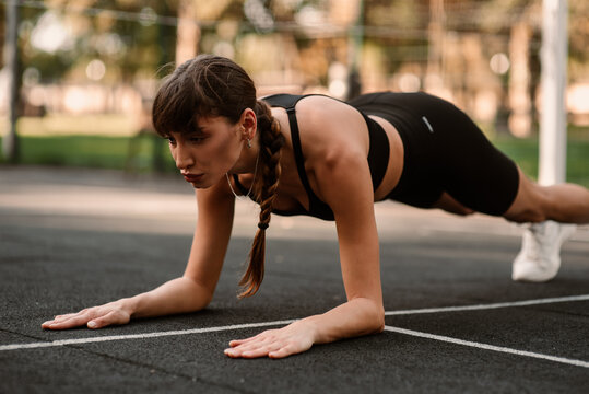 A young female trainer performs a fitness compression exercise. The girl is working out outdoors. Healthy lifestyle.