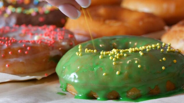 Large multi-colored fresh fried donuts in a row on a table. A beautiful donut with green icing is sprinkled with a special colored powder for decoration of sweets