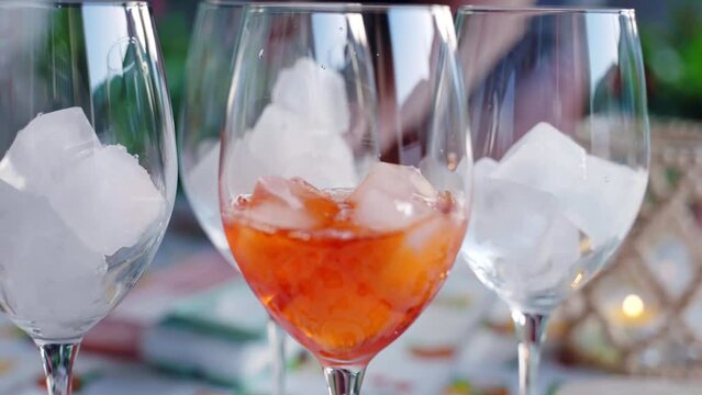 Process of traditional Italian aperol spritz preparation under the open air friends party, bartender pouring aperol into the wine glasses with ice cubes, refreshing aperol spritz cocktail, fizzy