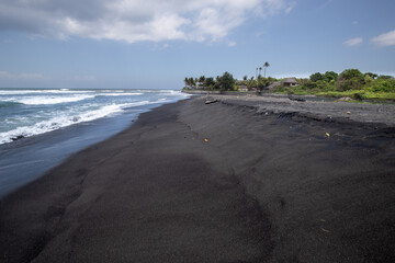 Black sand beach in Bali, natural with temples, boats (jukung) and waves at sunrise. Tropical environment in Indonesia in the morning
