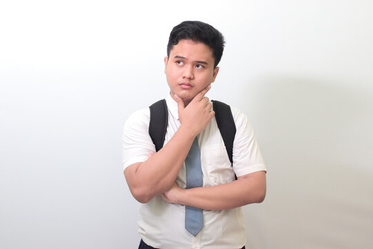 Indonesian senior high school student wearing white shirt uniform with gray tie and thinking about question with hand on chin. Isolated image on white background