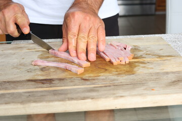 Slicing piece of ham with kitchen knife on wooden cutting board