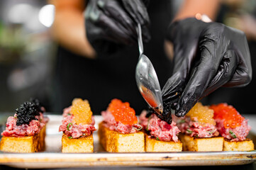 Chef cook hand cooking Canape with brioche, Raw beef meat tartar, caviar at the restaurant kitchen - obrazy, fototapety, plakaty