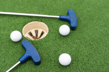 Mini-golf clubs and balls of different colors laid on artificial grass