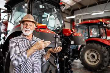 Farmer holding spare parts for tractor machine. Servicing and maintenance of agricultural machinery. - obrazy, fototapety, plakaty
