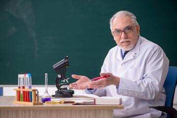 Old male chemist teacher sitting in the classroom