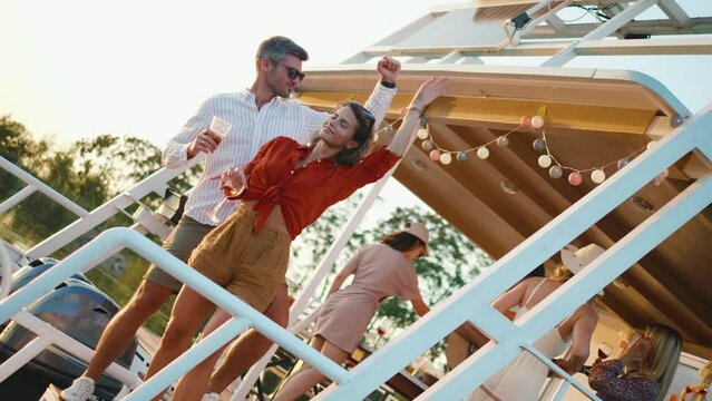 Group of young people dancing and toasting on a catamaran at sunset