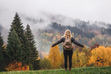 Woman gains energy and improves her mental health from nature in the mountains while hiking in an autumn forest - obrazy, fototapety, plakaty