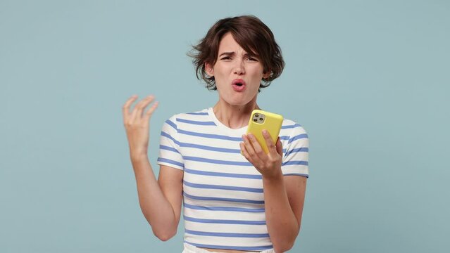Sad upset young woman wearing striped t-shirt casual clothes hold use mobile cell phone swear read bad fake news unexpected rumor has some problem isolated on pastel plain light blue cyan background