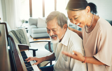 Fototapeta premium Senior couple playing piano for music in living room for bonding, entertainment or having fun. Happy, smile and elderly Asian man and woman in retirement enjoying keyboard instrument at modern home.