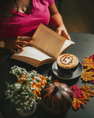 Girl reading book with Halloween cappuccino coffee with a scary spooky pumpkin latte art and decorations