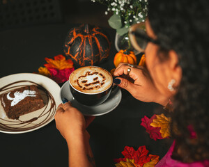 Girl holding a Halloween cappuccino coffee with a scary spooky pumpkin latte art and decorations