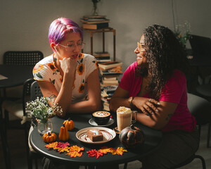 Cool girls have fun in Halloween coffee shop drinking cappuccino coffee with a scary spooky pumpkin decorations