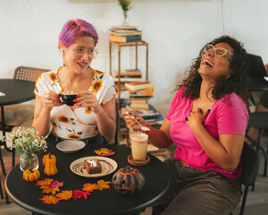 Cool girls have fun in Halloween coffee shop drinking cappuccino coffee with a scary spooky pumpkin decorations