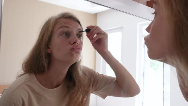 Beautiful woman making up by the mirror in hotel room , brushing eyebrows